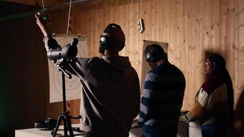 Firing range client doing shooting activity next to friends, zooming to check if he shot bullseye. Person analyzing targets shot using magnifying lens, comparing results with mates, camera A video