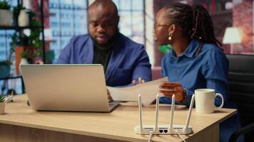 Black irritated man and woman rebooting their wireless router and checking network settings, feeling angry with the struggles to resolve an internet outage disrupting their tasks. Camera A. video