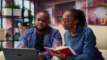 Mature people overseeing schedule and planning activities at coffee table, working on time management with online tools. Couple utilizing a notebooks and taking handwritten notes. Camera B. video