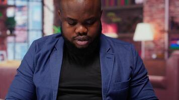 Teleworker at home office editing documents on his personal laptop, submitting reports and files before deadline. Black freelancer managing digital paperwork within the work platform. Camera b. video