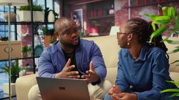 African american young freelancers on couch sharing a business idea, using modern technology and tools to analyze trends and boost success. Couple improving workflow efficiently. Camera A. video