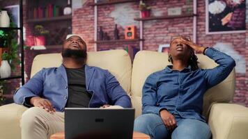 African american couple laying back on the couch and relaxing, feeling extremely tired and working under pressure. Sleepy people dealing with burnout and workload, freelancers with anxiety. Camera B. video