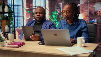 African american freelancers at home focused on online research and surfing the internet, utilizing a laptop and a tablet for telework and staying connected in a digital world. Camera A. video