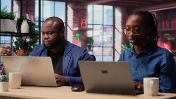 African American man and woman sit at a stylish home office, brainstorming ideas for their digital business, using modern technology to improve communication and project efficiency. Camera B. video