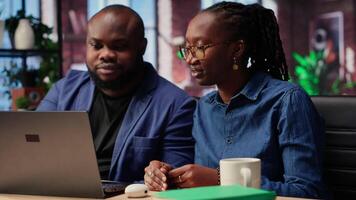 African american couple using ear buds to listen to a podcast or attend a webinar, hearing the online discussion on a web platform. Self employed man and woman spend time at the desk. Camera B. video