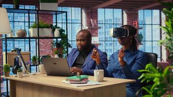 Self employed couple navigates remote work with advanced technology, young man explores 3D simulations through a VR headset. AI, metaverse and innovation in modern careers. Camera A. video