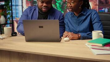African american couple using ear buds to listen to a podcast or attend a webinar, hearing the online discussion on a web platform. Self employed man and woman spend time at the desk. Camera A. video