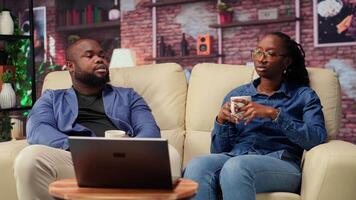 Happy people relaxing together on their comfortable sofa enjoying tea and casual conversation, laughing during leisure time. Affectionate bond and warmth make for a heartwarming lifestyle. Camera B. video