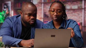 Freelancers filling in spreadsheets on laptop by entering data from report papers, analyzing figures at the end of the month. African american man and woman working from home. Camera B. video