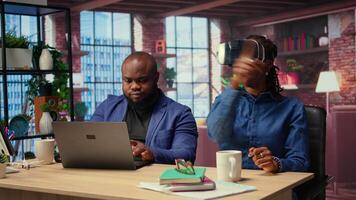 African American woman interacts with VR while her boyfriend completes the 3D animation on a laptop. Freelancers couple integrating artificial intelligence and creativity. Camera A. video