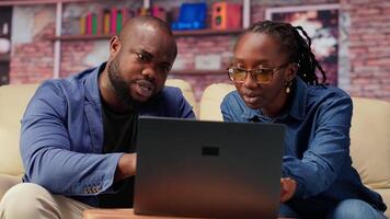 Freelancer couple doing research by reading articles and data driven papers at home, collecting information for a new project. People multitasking and studying online reports on sofa. Camera B. video