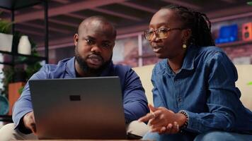 African american people on the sofa discussing a freelance strategy, researching marketing trends and online data from analytics tools to create a growth report. Remote efficiency. Camera B. video