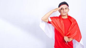 Portrait of Indonesian Man with Salute Pose and Red and White Flag Attribute on White Background photo