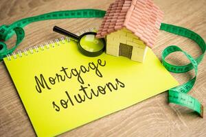 Mortgage Solutions concept. Assistance in purchasing a new home, refinancing existing mortgages and reduce their monthly payments. Real estate and loan rates. Notes and miniature house photo