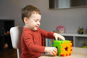 A cute happy little toddler boy of two years old sits at a children's table and plays with multi-colored sorter. Educational logic toys for children. Soft selective focus photo