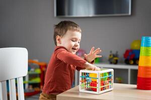 A cute little toddler boy of two years old plays with multi-colored balls and sits at a children's table in his room. photo