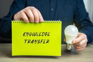 Knowledge transfer concept. Transferring knowledge from one part of the organization to another and the providing of inputs to problem solving. Businessman holding a notepad and idea light bulb photo