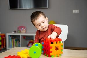 A cute attentive little toddler boy of two years old sits at a children's table photo