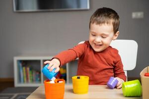 A happy smiling cute little toddler boy of two years old sits at a children's table and plays with multi-colored pyramids in his room. Educational toys for children. Soft selective focus photo