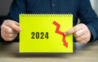 2024 and down arrow. Economic crisis and recession. Bankruptcy, finance crisis and forecasting. Analysis and analytics. Notepad in the hands of a businessman photo