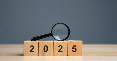 Wooden blocks with the inscription 2025. Setting goals and objectives for the new year. Planning, business management and strategy concept. Trends and ideas. Vision. Magnifying glass photo
