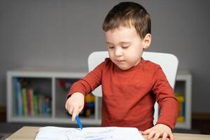 A cute attentive little toddler boy of two years old draws with markers in the album in the children's room at home. Educational activities for kids photo
