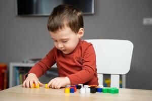 A cute little toddler boy of two years old sits at a children's table and plays with colorful cubes. Educational logic toys for children. Soft selective focus photo