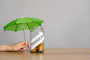 Bank of coins with the inscription Pension and green umbrella. Retirement Insurance concept. Financial support and regular payments to people after retirement. Business and finance photo