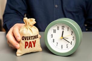 A man holds a money bag with overtime pay near a clock. Concept of additional compensation payment and incentive to work overtime. Wage increases, bonuses, extra hours, payroll benefits for hard work photo