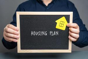 Businessman holding a board with the inscription Housing plan and house sticker. House project, drawings that are needed to build a house or apartment. real estate concept photo