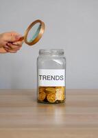 Bank of coins with the inscription Trends and magnifying glass. Analysis popular and relevant topics. New ideological trends of fashion. Recent and latest trend. Business and finance. Investments photo