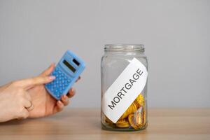 Bank of coins Mortgage and hand with calculator. The accumulation of money to pay interest rates on mortgages. Buying a property in debt. Take credit for housing. Mortgage tax and loan concept. photo