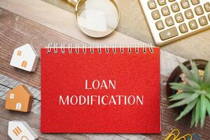 Loan modification concept - change made to the terms of an existing loan by a lender. Business and finance concept. Inscription on a notepad, miniature houses and a magnifying glass photo