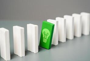 Domino with a green light bulb peeking out from a row. Concept of a good idea waiting for its time. Hidden opportunity, an innovative idea waiting for the right moment. Success, breakthrough solutions photo
