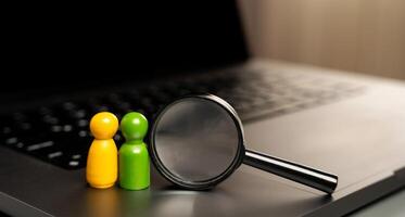 A figurine of people in the form of a pair of lovers stands on the keyboard near a magnifying glass. The concept of finding a soul mate and love online. photo