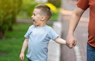 A happy three and a half years son walks hand in hand with his dad in the park on a sunny summer day. Family fun time and leisure. photo
