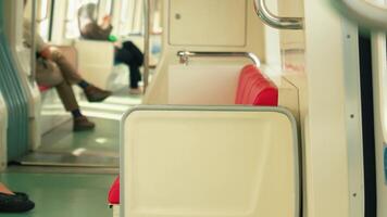 Interior view of a subway train with empty red seats and passengers in the background. The floor is green, and the lighting is bright video