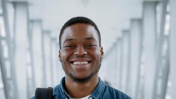 A young African American man is smiling confidently as he walks through an airport terminal. The bright, spacious indoor environment reflects a sense of excitement and adventure. video