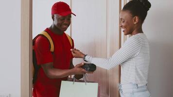 A man in a red cap and backpack delivers a package to a woman in her apartment. They exchange smiles, creating a friendly atmosphere in this home setting. video