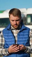 A truck driver speaks on smartphone while standing in front of parked trucks video