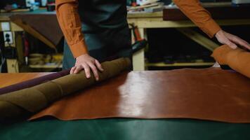 Skilled artisan unrolling a fine leather sheet, preparing for the next stage of creating bespoke leather goods video