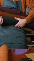 Skilled craftsman holding a roll of high-quality leather, preparing materials for crafting bespoke handmade leather goods in a professional workshop video