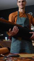Skilled craftsman holding a roll of high-quality leather, preparing materials for crafting bespoke handmade leather goods in a professional workshop video