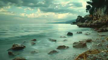 Serene coastal landscape with gentle waves lapping against rocky shore under cloudy sky photo