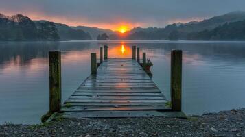 Serene sunset over a tranquil lake with a wooden dock leading into the water and hills in background photo