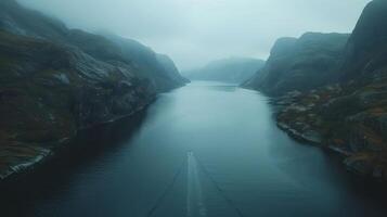 Serene Aerial View of a Narrow Fjord with a Boat Navigating Through Misty Mountains photo