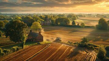Aerial view of a tractor plowing golden fields at sunset, surrounded by lush trees and distant homes photo