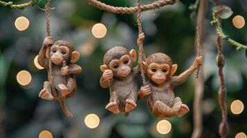 Three playful monkey figurines hanging from ropes against a blurred green background with lights photo