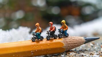 Miniature cyclists riding on a pencil in a snowy landscape with blurred background photo