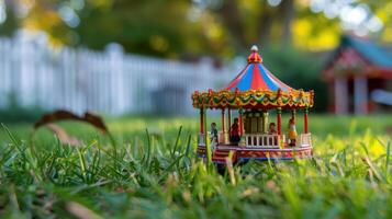 Miniature carousel on grass with a blurred background of a white fence and trees photo